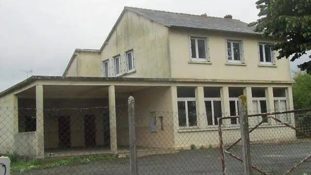 L'ancienne école de Chaumeré : un bâtiment de deux niveaux aux murs crème, avec un préau ouvert, derrière un grillage
