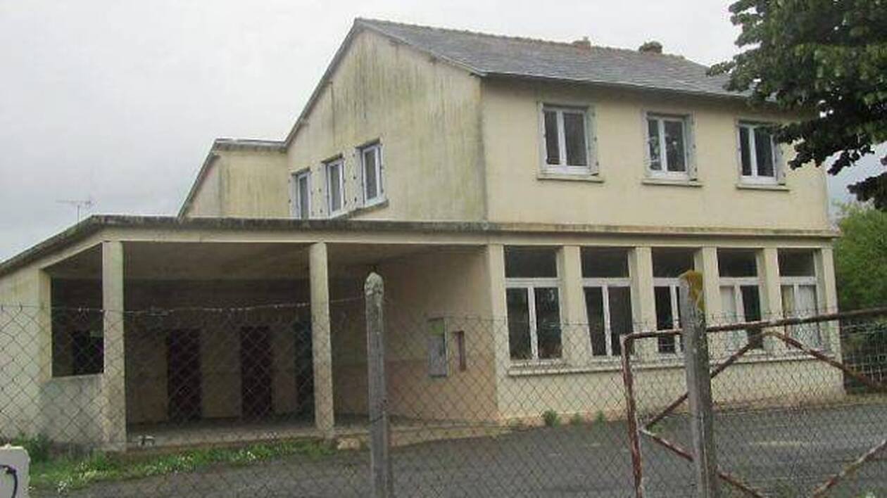 L'ancienne école de Chaumeré : un bâtiment de deux niveaux aux murs crème, avec un préau ouvert, derrière un grillage