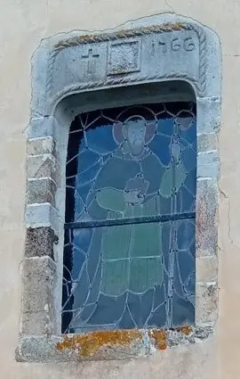Fenêtre à vitrail de l'église, au-dessus de la porte ouest : son linteau de pierre porte une croix et la date 1766