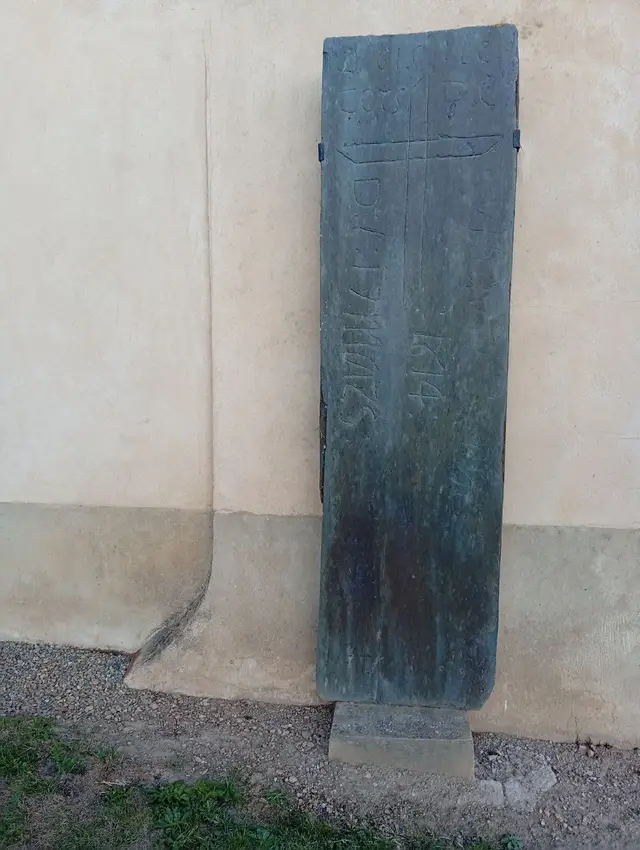 Pierre tombale ancienne gravée d'une croix et de la date 1614, appuyée contre le mur de l'église
