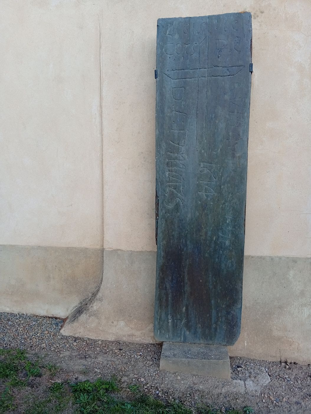 Pierre tombale ancienne gravée d'une croix et de la date 1614, appuyée contre le mur de l'église
